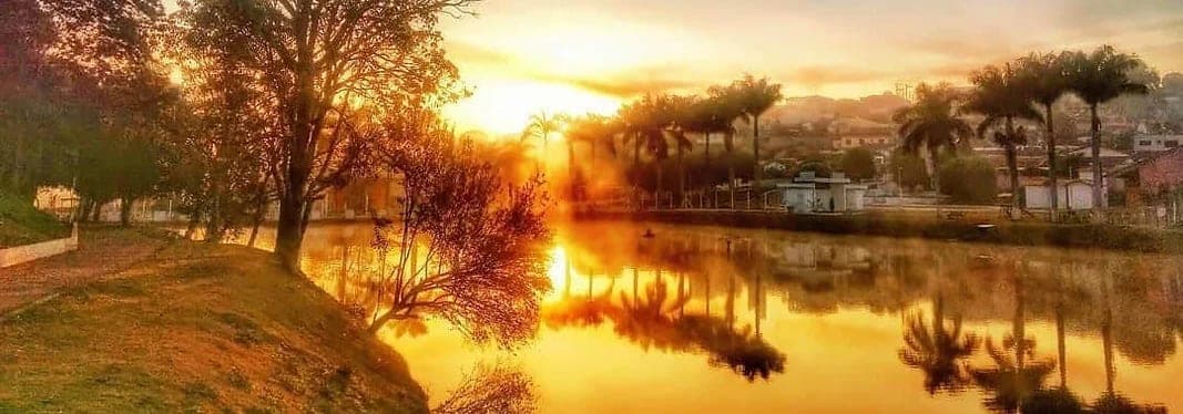 Vista de Carvalhópolis ao entardecer, com o lago e as palmeiras refletidos na água.